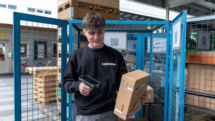 Liebherr employee scanning a packaged component with a handheld device for incoming goods inspection in the logistics area