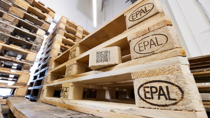 Wooden EPAL pallets with a QR‑coded block are stacked in a storage area.